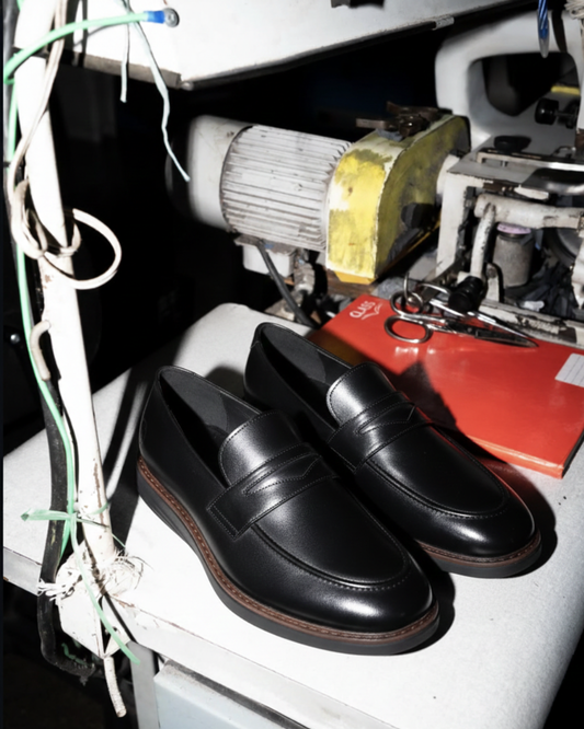 Black penny loafers in workshop setting showing handcrafted quality